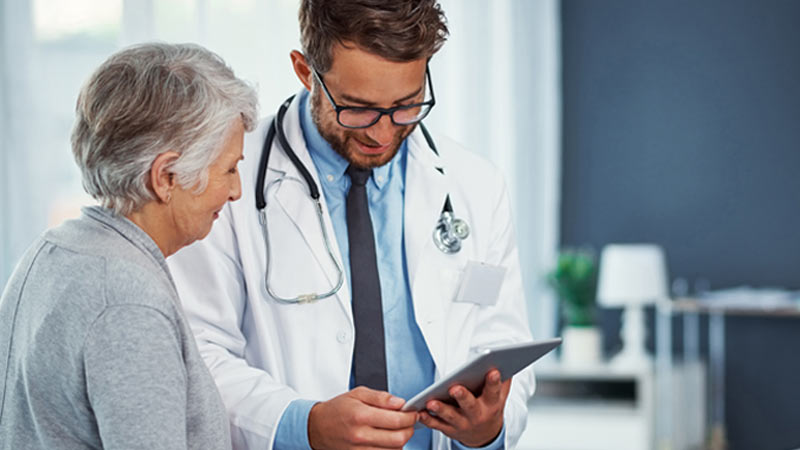 Médico e paciente sénior avaliam ficha num ambiente de hospital